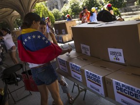 A woman, with a Venezuela flag over her shoulders, casts her ballot during a symbolic referendum in Madrid, Sunday, July 16, 2017. Venezuela's opposition called for a massive turnout Sunday in a symbolic rejection of President Nicolas Maduro's plan to rewrite the constitution, a proposal that's escalating tensions in a nation stricken by widespread shortages and more than 100 days of anti-government protests. White sheets on the boxes read in Spanish: "Popular referendum" and "People decide!". (AP Photo/Francisco Seco)