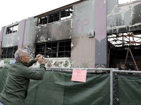 ** HOLD FOR OVERNIGHT MOVEMENT ** FILE - In this Dec. 13, 2016 file photo, a man takes cell phone photos at the scene of a warehouse fire in Oakland , Calif. The man blamed for the nation's deadliest structure fire in more than 14 years will be arraigned in Northern California on 36 counts of involuntary manslaughter. Derick Almena is scheduled to enter a plea Thursday, June 8, 2017. The 47-year-old was arrested and charged Monday with creating a deadly firetrap by illegally converting an Oakland warehouse into a party space and housing. (AP Photo/Marcio Jose Sanchez, File)