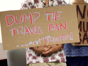 FILE- In this June 30, 2017, file photo, critics of President Donald Trump's travel ban hold signs during a news conference with Hawaii Attorney General Douglas Chin in Honolulu. A federal judge in Hawaii on Thursday, July 6, left Trump administration rules in place for a travel ban on citizens from six majority-Muslim countries. U.S. District Court Judge Derrick Watson denied an emergency motion filed by Hawaii asking him to clarify what the U.S. Supreme Court meant by a "bona fide" relationship in its ruling last month. (AP Photo/Caleb Jones, File)