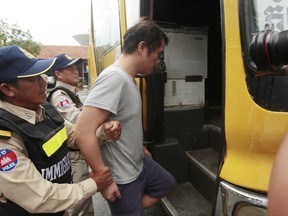 A Chinese national arrested over an alleged internet scam is escorted by police officers to be deported at the immigration office in Phnom Penh, Cambodia, Wednesday, July 26, 2017. Police says they have deported over a dozen Chinese nationals in an alleged internet scam back to China complying with demands from Beijing. (AP Photo/Heng Sinith)