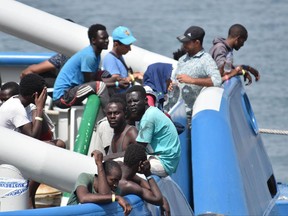 Migrants stand on the deck of the Swedish Navy ship Bkv 002, as they wait to disembark in the Sicilian harbor of Catania, Italy, Saturday, July 1, 2017. The Swedish ship carried 650 migrants rescued in various operations in the Mediterranean Sea and the dead bodies of seven men and two women, authorities said. (Orietta Scardino/ANSA via AP)