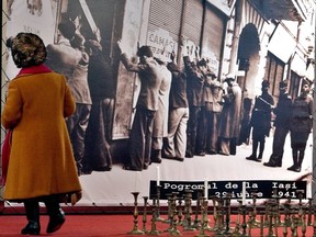 FILE - In this Jan. 25, 2004 file photo, an elderly woman passes near a picture of Romanian Jews rounded up by authories in Iasi, Romania, in 1941, at a holocaust memorial exhibition in Bucharest Romania. The exhibition, displaying pictures of Romanian Jews killed in death camps and various of their personal belongings, remembers those deported or killed between 1933 and 1945. The Conference on Jewish Material Claims Against Germany says Wednesday, July 12, 2017 about 1,000 living survivors of Nazi persecution in Romania are now eligible for compensation in a new agreement reached with Berlin.  (AP Photo/Vadim Ghirda,file)