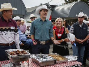 Prime Minister Justin Trudeau, centre, tries to drum up customers as he serves pancakes at a Stampede breakfast in Calgary, Alta., Saturday, July 15, 2017. THE CANADIAN PRESS/Jeff McIntosh