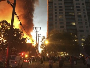 In this photo provided Emily Lesk, a large fire, left, burns at a building under construction Friday, July 7, 2017, in Oakland, Calif. The fire broke out around dawn Friday at a seven-story building under construction, forcing evacuations of people nearby, and sending flames high into the air. Officials say the fire is contained. No injuries have been reported. (Emily Lesk via AP)