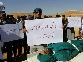 This Tuesday, July 4, 2017 photo, shows Syrian refugees holding placards as they stand by the body of a deceased Syrian man, in the town of Arsal, near the Syrian border, in northeast Lebanon. Anger mounted among Syrians in Lebanon Wednesday with at least one Syrian opposition group and an international human rights organization calling for a quick investigation after the death of at least four Syrians in Lebanese army custody. The placard in Arabic, center, reads, "For what crime was he killed? ... In Arsal," and at right, "We haven't come to Lebanon for tourism," and left, "Take us to Jarablus [Syria]."  (AP Photo)