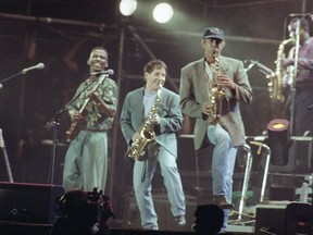 FILE - In this Aug. 16, 1991 file photo, Paul Simon, center, plays a finale with lead guitarist Ray Phiri, left, and actor-comedian Chevy Chase on the saxophone in New York's Central Park. Ray Phiri, a South African jazz musician who founded the band Stimela and performed on Paul Simon's Graceland tour, died of cancer on Wednesday July 12, 2017 at the age of 70. (AP Photo/Malcolm Clarke, File)