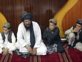 In this photo taken on Tuesday, July 25, 2017, Mohammed Naseer, with black turban, and three children wait for their food in the prayer area of a Pizza Restaurant in Kabul, Afghanistan. Mohammed Naseer spent several weeks arranging for his son, a nephew and several other children from his district of Ander in Ghazni province to go to Quetta to study the Quran. (AP Photos/Massoud Hossaini)