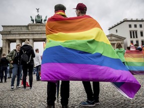 CORRECTS TO  GERMAN PRESIDENT SIGNED  LEGISLATION THURSDAY JULY 20, 2017 - FILE - In this June 30, 2017 file photo, men with rainbow flags stand in front of the Brandenburg Gate at an event organized by the Social Democrats to celebrate the legalization of same-sex marriage in Berlin. Germany's president has signed legislation Thursday July 20,  2017  legalizing gay marriage, paving the way for it to take effect this fall.Lawmakers  approved the bill on June 30 in its last session before Germany's September election. (Michael Kappeler/dpa via AP,file)