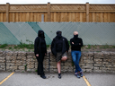 Three masked people stand outside a memorial for Toronto lawyer Barbara Kulaszka at the Richview branch of the Toronto Public Library on July 12,  2017.
