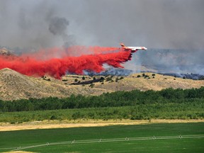 In this Sunday, July 23, 2017, photo, a plane drops a defensive line of retardant on a wildfire near Sand Springs, Mont. Massive wildfires burning in eastern Montana have destroyed at least a dozen homes and led ranchers to cut escape routes in fences for cattle as the powerful blazes jump rivers, roads and bulldozer-cleared fire breaks. (Rebecca Noble/The Billings Gazette via AP)