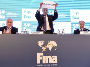 President of the International Swimming Federation, FINA, Julio C. Maglione raises a sheet of paper bearing the name of the Hungarian capital between Sports Minister of Tatarstan Vladimir Leonov, left, and FINA Vice President Husain Al-Musallam of Kuwait during a press conference held after the FINA Bureau vote deciding Kazan, Tatarstan, and Budapest as host cities of the 25m pool world championships in 2022 and 2024, respectively, during the FINA World Aquatics Convention in Budapest, Hungary, Monday, July 17, 2017. (Zsolt Szigetvary/MTI via AP)