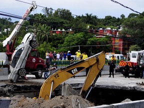 Rescue workers use a crane to lift a vehicle that drove into a sinkhole on a highway in Cuernavaca, Mexico, Wednesday, July 12, 2017. A father and son were killed when the deep sinkhole swallowed their car on Wednesday morning. Civil protection rescuers reached the rubble-covered Volkswagen Jetta lying on its roof at the bottom of the hole in the afternoon, after working for more than eight hours on the closed section of road. (AP Photo/Tony Rivera)