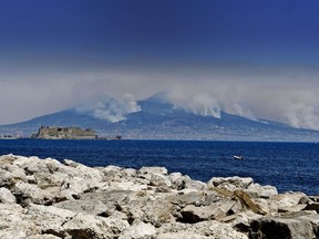 Smoke rises from wild fires burning on the slopes of Mt. Vesuvius volcano as the Castel dell'Ovo castle in seen in the foreground, in Naples, Italy, Wednesday, July 12, 2017.  Firefighters are battling wildfires throughout southern Italy, including along the slopes of the volcano Mount Vesuvius near Naples. Wildfires have been raging for days, and Italy's civil protection agency on Tuesday said it was responding with helicopters to 18 blazes, including four in Campania, the region which includes Naples, and two each in Sicily and Basilicata.  (Ciro Fusco/ANSA via AP)
