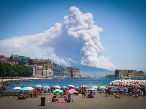 Smoke rises from wild fires burning on the slopes of Mt. Vesuvius volcano as people sun bathe on a beach with the Castel dell'Ovo castle in the background right, in Naples, southern Italy, Tuesday, July 11, 2017. High temperatures and no rainfall contribute to the risk of wild fires in the summer months.  (Ciro Fusco/ANSA via AP)
