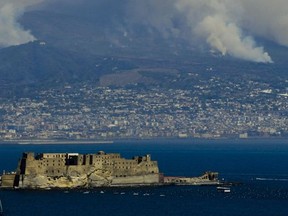 Smoke rises from wild fires burning on the slopes of Mt. Vesuvius volcano as the Castel dell'Ovo castle in seen in the foreground, in Naples, Italy, Wednesday, July 12, 2017.  Firefighters are battling wildfires throughout southern Italy, including along the slopes of the volcano Mount Vesuvius near Naples. Wildfires have been raging for days, and Italy's civil protection agency on Tuesday said it was responding with helicopters to 18 blazes, including four in Campania, the region which includes Naples, and two each in Sicily and Basilicata.  (Ciro Fusco/ANSA via AP)