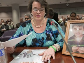 FILE- In this Jan. 28, 2013, file photo, Veronique Pozner places her hand next to artwork made by her son Noah's before testifying before a hearing of a legislative subcommittee reviewing gun laws at the Legislative Office Building in Hartford, Conn. The town of Newtown and its Board of Education asked a judge to throw out the wrongful death lawsuit filed by the parents of two children killed during the Sandy Hook shootings in December 2012. The lawsuit was brought by the estates of 6-year-olds Noah Pozner and Jesse Lewis. (AP Photo/Jessica Hill, File)