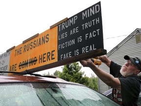 Jim Girvan attaches protest signs to his car, not far from Trump National golf course, where President Trump is attending the Women's US Open tournament, Saturday, July 15, 2017 in Branchburg, N.J. Girvan and others are planning protests throughout the weekend. (AP Photo/Mel Evans)