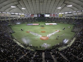 FILE - In this March 28, 2012, file photo, flags of the United States and Japan are carried during the opening ceremony at a season-opening baseball game between the Oakland Athletics and the Seattle Mariners at Tokyo Dome in Tokyo. Major League Baseball plans to start the 2019 and 2020 seasons in Asia and play regular-season games in England in June of both years. The collective bargaining agreement reached in November was finalized and sent to the clubs Friday, July 28, 2017. (AP Photo/Shizuo Kambayashi, File)