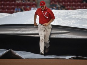 A grounds crew member helps pull a tarp over the infield during a rain delay before a baseball game between the Cincinnati Reds and the Miami Marlins, Friday, July 21, 2017, in Cincinnati. (AP Photo/John Minchillo)