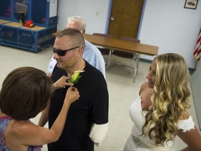 Tina Reinke pins a flower onto Leechburg Police Chief Mike Diebold as his bride, Danielle Reinke looks on, at the Leechburg Volunteer Fire House, Wednesday,  July 12, 2017 in Leechburg, Pa. The 39-year-old chief who is also licensed to run his own fireworks business, was injured when a shell exploded June 24, losing his left hand and lower arm. Diebold was released from a Pittsburgh hospital a week before the wedding and eventually hopes to resume his police duties wearing a prosthetic limb. (Nate Smallwood/Pittsburgh Tribune-Review via AP)