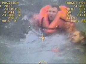 In this still image from video taken on Monday, July 24, 2017, by the Coast Guard, the captain of the fishing vessel Grayling, left, rescues one of his crewmen after the vessel capsized in the Kupreanof Strait near Raspberry Island, Alaska,. The captain jumped into cold, choppy waters to save two of his crew members after their vessel capsized off the Alaska coast. (William Colclough/U.S. Coast Guard via AP)