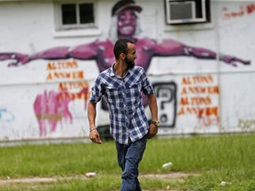 In this June 27, 2017 photo, Abdullah Muflahi walks outside his Triple S Food mart in front of a mural of Alton Sterling in Baton Rouge, La. Little has changed in this poverty-stricken neighborhood since Sterling was shot by police one year ago, a frustrating fact of life for residents and business owners who had hoped a national spotlight on their problems could erode racial tensions and improve police relations in Louisiana's capital. (AP Photo/Gerald Herbert)