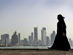 FILE- In this May 14, 2010 file photo, a Qatari woman walks in front of the city skyline in Doha, Qatar. Qatar likely faces a deadline this weekend to comply with a list of demands issued to it by Arab nations that have cut diplomatic ties to the energy-rich country, though its leaders already have dismissed the ultimatum. (AP Photo/Kamran Jebreili, File)