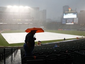 A spectator takes cover under an umbrella during a rain delay before a baseball game between the Tampa Bay Rays and the Baltimore Orioles in Baltimore, Saturday, July 1, 2017. (AP Photo/Patrick Semansky)