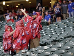 A few fans stand covered by ponchos as others take shelter beneath an overhang during a light shower that delayed the start of a baseball game between the Boston Red Sox and Texas Rangers on Wednesday, July 5, 2017, in Arlington, Texas. (AP Photo/Tony Gutierrez)