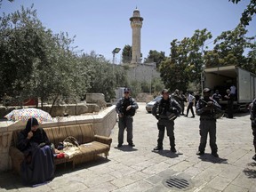 Israeli border police officers stand guard as a Palestinian woman sits outside the Al Aqsa Mosque compound, in Jerusalem, Sunday, July 16, 2017.