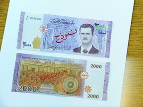 In this photo released by the Syrian official news agency SANA, the new bank note of 2,000 Syrian Lira, ($3.9), is seen during a press conference for the Central Bank Governor Duraid Durgham in Damascus, Syria, Sunday, July 2, 2017. The notes are the first time the face of President Bashar Assad appears on the Syrian currency since he took office 17 years ago. (SANA via AP)