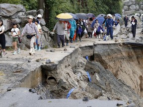In this July 6, 2017 photo,  local residents walk on a damaged road to a safer place following the flooding caused by heavy rain in Asakura, Fukuoka prefecture, southwestern Japan. Troops worked Thursday to rescue hundreds of people stranded by flooding in southern Japan. (Takuto Kaneko/Kyodo News via AP)