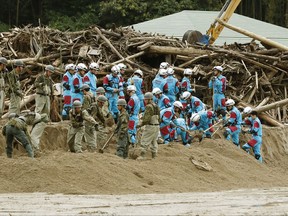 Japan's Self-Defense Forces members and police officers, in blue, remove mud at the site of a landslide in Asakura, southwestern Japan, Wednesday, July 12, 2017. Prime Minister Shinzo Abe is visiting disaster-stricken southernmost main island of Kyushu, cutting short a European trip following the G-20 summit in Germany. He will go to the hard-hit cities of Hita in Oita prefecture and Asakura and Toho in Fukuoka prefecture. (Kyodo News via AP)