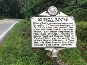 In this June 25, 2017 photo a sign at the edge of Seneca Rocks in eastern West Virginia, between the hamlet's general store/restaurants and its climbing cliff, describes some of its natural and human history. (AP Photo/Michael Virtanen)