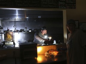 Aaron Howe cooks in the dark kitchen at the Island Convenience Store in Rodanthe on Hatteras Island, N.C.,  on Friday, July 28, 2017.   An estimated 10,000 tourists face a noon deadline Friday for evacuating the island on North Carolina's Outer Banks after a construction company caused a power outage, leaving people searching for a place to eat, stay cool or to resume interrupted vacations. Howe says it is the only place in town to get a meal.  (Steve Earley  /The Virginian-Pilot via AP)