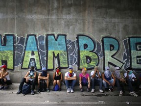 Anti-government demonstrators sit under a bridge that has graffiti written in Spanish that reads "Hunger," during a protest in Caracas, Venezuela, Saturday, July 1, 2017. Demonstrators are taking the the streets after three months of continued protests that has left dozens dead and seen the country's chief prosecutor Luisa Ortega barred from leaving the country and her bank accounts frozen, by the Supreme Court following her mounting criticisms of President Nicolas Maduro. (AP Photo/Ariana Cubillos)