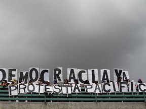 Anti-government demonstrators protest with a sign that reads in Spanih "Democracy Now. Peaceful Protest" in Caracas, Venezuela, Saturday, July 1, 2017. Demonstrators are taking the the streets after three months of continued protests that has left dozens dead and seen the country's chief prosecutor Luisa Ortega barred from leaving the country and her bank accounts frozen, by the Supreme Court following her mounting criticisms of President Nicolas Maduro. (AP Photo/Ariana Cubillos)