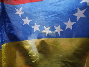 An anti-government demonstrator is seen behind a Venezuelan national flag during a protest in Caracas, Venezuela, Sunday, July 9, 2017. Opposition demonstrators are commemorating 100 days of continued street protests and celebrating that opposition leader Leopoldo Lopez was released from prison and sent home under house arrest. (AP Photo/Ariana Cubillos)