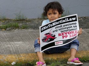 A girl sits with a placard as demonstrators protest President Rodrigo Duterte's Martial Law declaration for the southern Mindanao region which was upheld by the supreme court, Friday, July 7, 2017, outside of the Philippine armed forces headquarters in Quezon city northeast of Manila, Philippines. The court upheld the legality of the Duterte's martial law declaration in a legal boost to a massive offensive that officials say may quell an uprising by Islamic State group-linked militants in a week's time at the earliest. (AP Photo/Bullit Marquez)