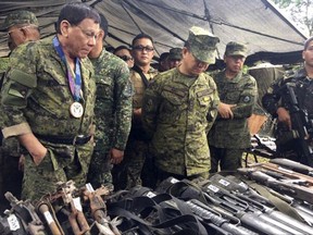 In this photo provided by the Armed Forces of the Philippines, Philippine President Rodrigo Duterte, left, clad in a camouflage uniform inspects firearms recovered from Muslim militants during his unannounced visit to Camp Ranao in Marawi city in southern Philippines Thursday, July 20, 2017. Duterte flew for the first time Thursday to the besieged southern city to cheer troops who have been trying to quell a nearly two-month uprising by Islamic State group-linked militants, who he warned were plotting to attack other cities. In the center is Armed Forces Chief Gen. Eduardo Ano. (Armed Forces of the Philippines via AP)