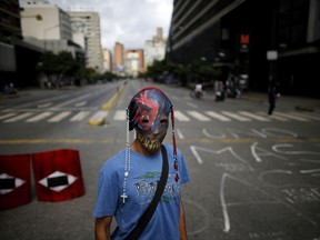 A demonstrator wearing a mask adorned with rosaries stands near a barricade during a 48-hour general strike beginning Wednesday in protest of government plans to rewrite the constitution in Caracas, Venezuela, Wednesday, July 26, 2017. President Nicolas Maduro is promoting the constitution rewrite as a means of resolving Venezuela's political standoff and economic crisis, but opposition leaders are boycotting it. (AP Photo/Ariana Cubillos)