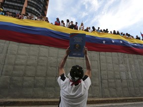 FILE - In this July 24, 2017 file photo, an anti-government demonstrator holds up an image of Venezuela's constitution during a tribute to those killed during protests against Venezuela's President Nicolas Maduro, in Caracas, Venezuela. Maduro has provoked international outcry and enraged political opponents by pushing for a special assembly tasked with rewriting the troubled South American nation's constitution. (AP Photo/Fernando Llano, File)