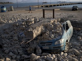 A man walks past a car crushed under rubble near the port of the Greek island of Kos on Saturday, July 22, 2017. Hundreds of residents and tourists on the eastern Greek island of Kos spent the night sleeping outdoors, on beach lounge-chairs, in parks and olive groves or in their cars, a night after a powerful earthquake killed two tourists and injured nearly 500 others across the Aegean Sea region, in Greece and Turkey. (AP Photo/Petros Giannakouris)