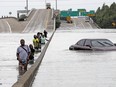 Evacuees wade down a flooded section of Interstate 610 as floodwaters from Tropical Storm Harvey rise Sunday, Aug. 27, 2017, in Houston.