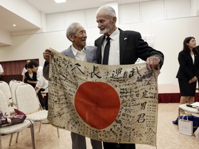Second World War veteran Marvin Strombo, right, and Tatsuya Yasue, an 89-year-old farmer, hold a Japanese flag with autographed messages which was owned by his brother Sadao Yasue, who was killed in the Pacific. A ceremony was held in Higashishirakawa this week to return the fallen soldier's calligraphy-covered flag to his family.