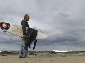 In this photo taken from video, Marcel Brunder, 37, holds his board as he looks out to sea after being attacked while surfing, Tuesday, Aug. 29, 2017, in the waters near Lorne, 140 kms. (90 miles) southwest of Melbourne, Australia.