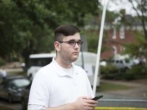 In this Saturday, Aug. 12, 2017, photo, James Alex Fields Jr. stands on the sidewalk looking at the procession of the clergy as they gathered at McGaffey park, ahead of a rally in Charlottesville, Va. Fields is accused of ramming his car into a crowd of counter-protesters Saturday in Charlottesville, killing 32-year-old Heather Heyer and injuring over a dozen others. (Eze Amos via AP)