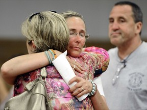 FILE - In this July 11, 2013 file photo, Scarlett Lewis, center, mother of Sandy Hook Elementary School shooting victim Jesse Lewis, hugs Lynn McDonnell, left, mother of victim Grace McDonnell, as Neil Heslin, right, father of Jesse Lewis watches after a public forum in Newtown, Conn. Lawyers for Lewis, Heslin and Leonard Pozner, father of Noah Pozner who also was killed in the school shooting, filed motions Tuesday, Aug. 15, 2017, in Danbury Superior Court seeking to see evidence that two teachers fatally shot in the massacre had access to keys that could have been used to lock their classroom doors. (AP Photo/Jessica Hill)