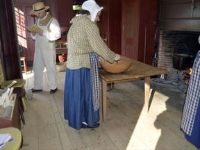 In this June 10, 2017 photo provided by Tracee Herbaugh, people dressed in period costumes prepare dinner in the "Boarding with the Bixbys" program at Old Sturbridge Village in Sturbridge, Mass. The process of preparing food generally took several hours in the early 19th century. In the evenings, families would eat "supper" on a table draped with a white cloth and lit by candlelight. (Tracee Herbaugh via AP)