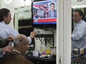 FILE - In this May 4, 2011 file photo, a Palestinian barber gives a customer a haircut as a TV set shows a demonstration in Egypt, on the Al Jazeera channel, at a barber shop in Jerusalem's Old city. Israel's communications minister said, Sunday, Aug. 6, 2017, that he wants to shut down pan-Arab broadcaster Al-Jazeera in the country. Ayoob Kara, of Prime Minister Benjamin Netanyahu's Likud party, said he wants the news network's press cards revoked and has asked cable providers to block their transmissions. (AP Photo/Sebastian Scheiner, File)